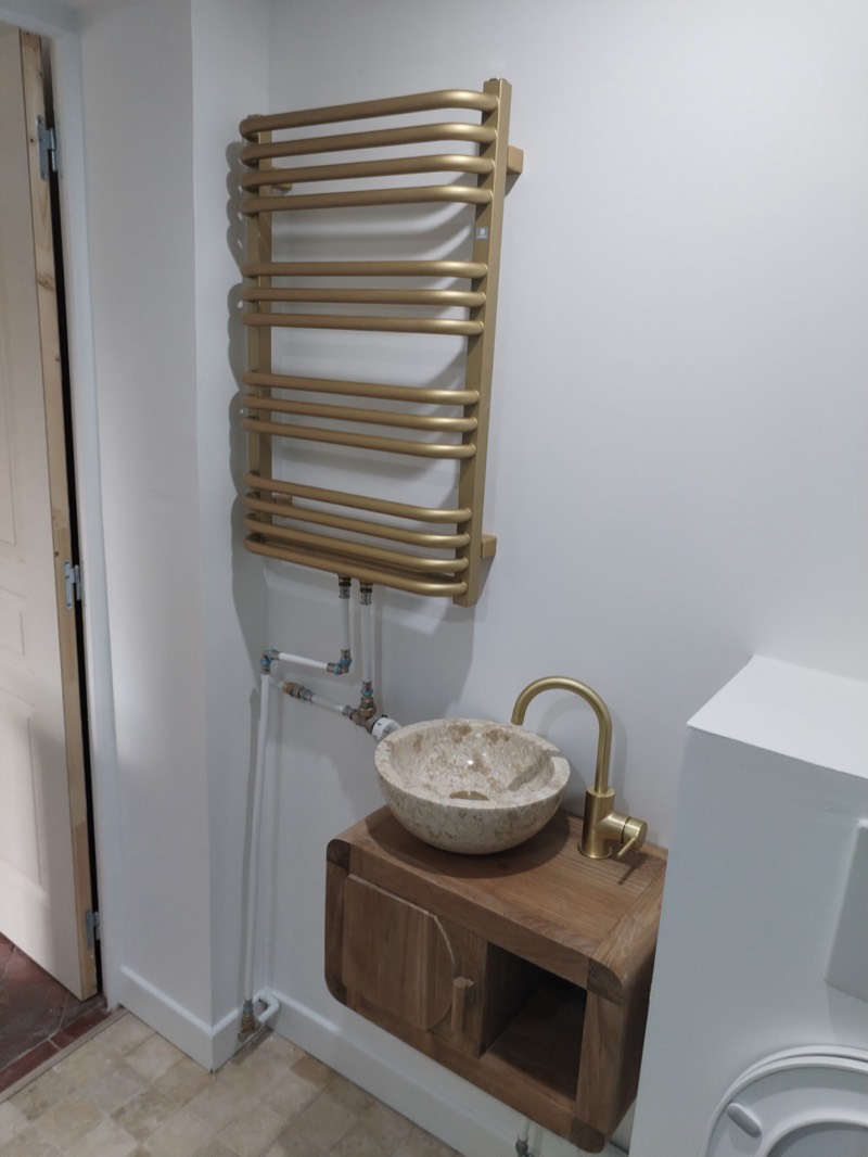 Salle d'eau rénovée : sèche-serviettes doré, vasque pierre sur meuble bois massif, robinetterie dorée