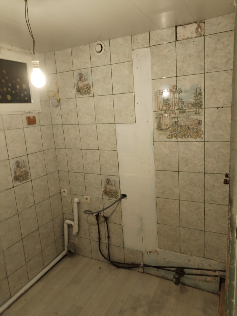 Avant : ancienne salle d'eau avec carrelage fleuri et plomberie apparente